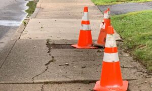 Boundary line survey relevance shown with cracked sidewalk and traffic cones marking street damage