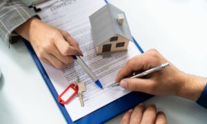 Homebuyers signing property documents with keys and house model during closing survey process