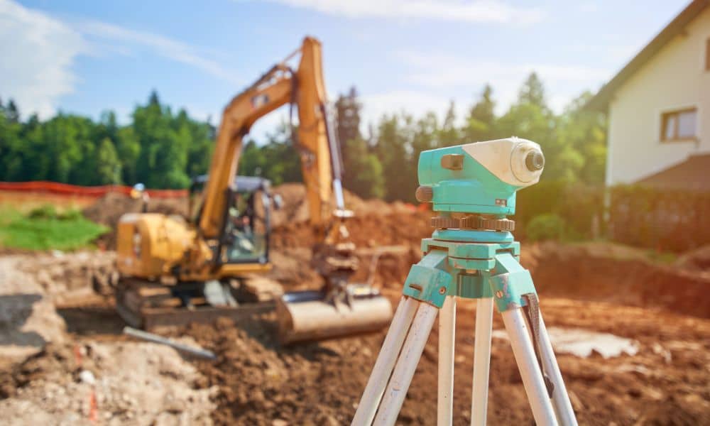 A construction surveyor using a leveling instrument on an active hillside construction site after rain and soil movement