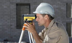 A surveyor using a tripod and total station to perform a construction survey on a building site