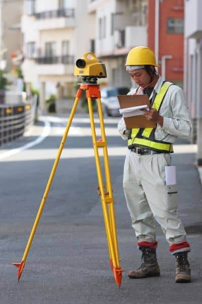 Boundary line surveyor using total station equipment to check property lines after street damage