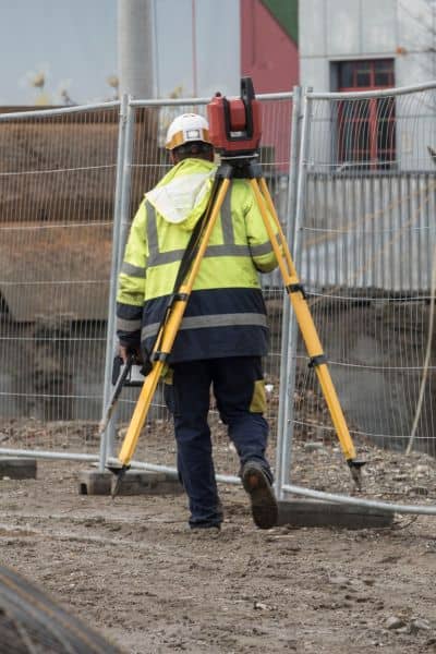 Licensed land surveyor using tripod equipment for an ALTA Land Title Survey on a rebuilding site after wildfire damage.
