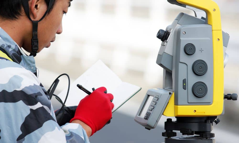 A land surveyor using a total station to collect measurements for a topo survey