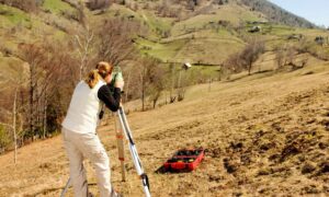 Land surveyor performing a topographic survey on a sloped hillside to measure elevation and terrain changes