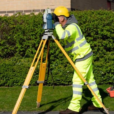 Licensed surveyor performing land surveying field measurements using a total station on site