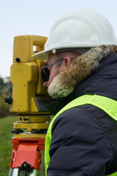 Surveyor using a total station to complete a land survey on a residential property site
