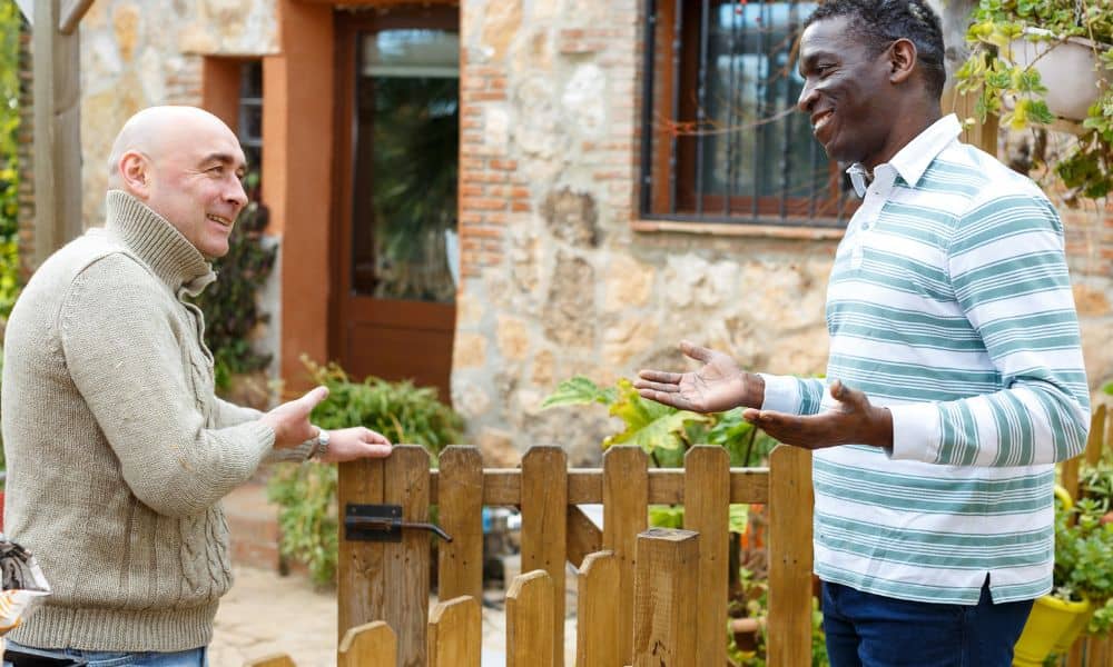 Two homeowners talking near a fence while discussing a property boundary with a local surveyor